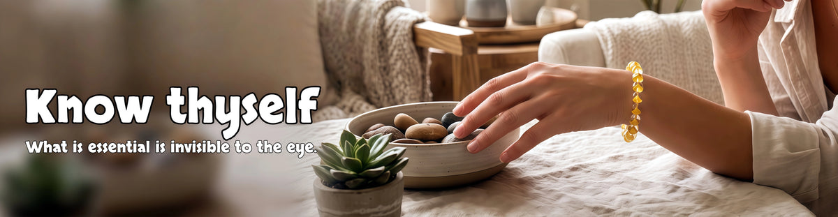 A person wearing a yellow crystal bracelet reaching toward a bowl of natural stones.